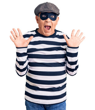 Senior handsome man wearing burglar mask and t-shirt celebrating crazy and amazed for success with arms raised and open eyes screaming excited. winner concept