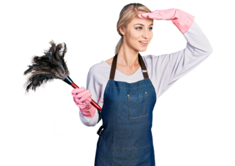 Beautiful young blonde woman wearing apron holding cleaning duster very happy and smiling looking far away with hand over head. searching concept.