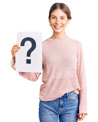Beautiful caucasian woman with blonde hair holding question mark looking positive and happy...