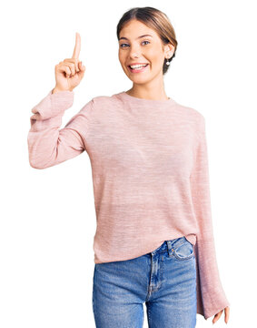 Beautiful caucasian woman with blonde hair wearing casual winter sweater pointing finger up with successful idea. exited and happy. number one.