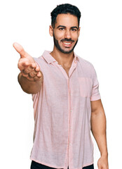 Hispanic man with beard wearing casual shirt smiling friendly offering handshake as greeting and welcoming. successful business.