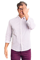 Young handsome man wearing business clothes and glasses covering one eye with hand, confident smile on face and surprise emotion.