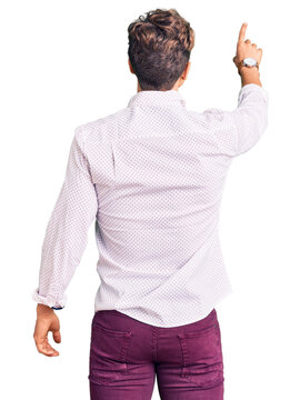 Young handsome man wearing business clothes and glasses posing backwards pointing ahead with finger hand