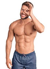 Fototapeta premium Young caucasian man standing shirtless doing ok gesture with hand smiling, eye looking through fingers with happy face.