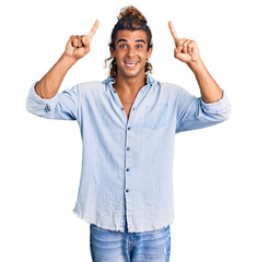 Young hispanic man wearing summer style smiling amazed and surprised and pointing up with fingers...