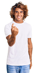 Young hispanic man wearing casual white tshirt beckoning come here gesture with hand inviting...
