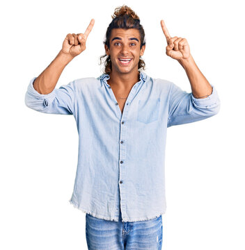 Young hispanic man wearing summer style smiling amazed and surprised and pointing up with fingers and raised arms.