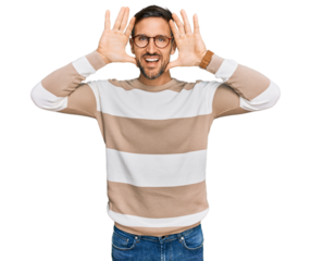 Handsome man with beard wearing casual clothes and glasses smiling cheerful playing peek a boo with hands showing face. surprised and exited