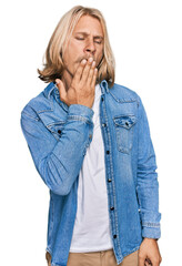 Caucasian man with blond long hair wearing casual denim jacket bored yawning tired covering mouth with hand. restless and sleepiness.