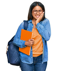 Young latin girl wearing student backpack and holding books laughing and embarrassed giggle...