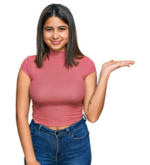 Young hispanic girl wearing casual t shirt smiling cheerful presenting and pointing with palm of hand looking at the camera.