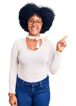 Young african american girl wearing casual clothes and glasses with a big smile on face, pointing with hand finger to the side looking at the camera.