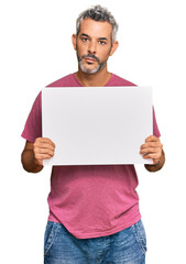 Middle age grey-haired man holding blank empty banner thinking attitude and sober expression...