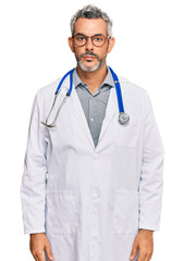 Middle age grey-haired man wearing doctor uniform and stethoscope with serious expression on face. simple and natural looking at the camera.