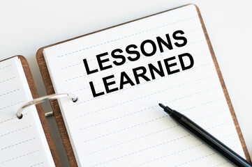 LESSONS LEARNED inscription on a notebook next to a black marker, a business concept