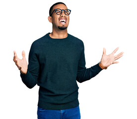 Young african american man wearing casual clothes and glasses crazy and mad shouting and yelling...