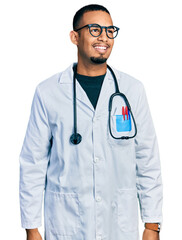Young african american man wearing doctor uniform and stethoscope looking away to side with smile...