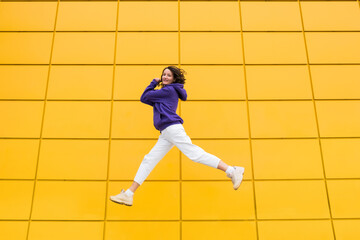 Happy positive woman in purple hoody have fun on yellow mall wall. Millennials girl with good mood...