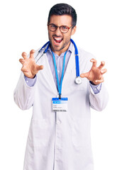 Young hispanic man wearing doctor uniform and stethoscope smiling funny doing claw gesture as cat,...
