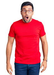 Young hispanic man wearing casual clothes and glasses scared and amazed with open mouth for...