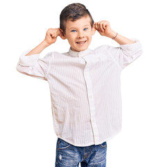Cute blond kid wearing elegant shirt smiling pulling ears with fingers, funny gesture. audition...