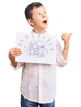 Cute blond kid holding scribble draw pointing thumb up to the side smiling happy with open mouth