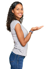 Young african american girl wearing casual clothes pointing aside with hands open palms showing copy space, presenting advertisement smiling excited happy
