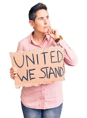 Young woman with short hair holding united we stand banner serious face thinking about question with hand on chin, thoughtful about confusing idea