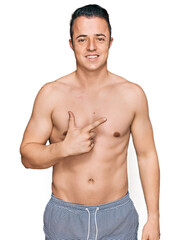 Fototapeta premium Handsome young man wearing swimwear shirtless cheerful with a smile on face pointing with hand and finger up to the side with happy and natural expression