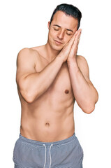 Fototapeta premium Handsome young man wearing swimwear shirtless sleeping tired dreaming and posing with hands together while smiling with closed eyes.
