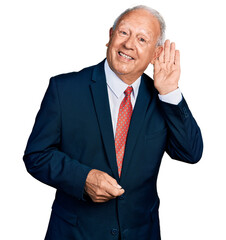 Senior man with grey hair wearing business suit and tie smiling with hand over ear listening and hearing to rumor or gossip. deafness concept.