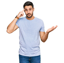 Young hispanic man wearing casual clothes confused and annoyed with open palm showing copy space and pointing finger to forehead. think about it.