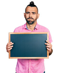 Hispanic man with ponytail holding blackboard puffing cheeks with funny face. mouth inflated with air, catching air.