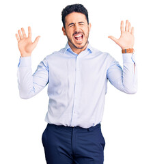 Fototapeta premium Young hispanic man wearing business clothes celebrating mad and crazy for success with arms raised and closed eyes screaming excited. winner concept