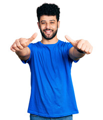 Young arab man with beard wearing casual blue t shirt approving doing positive gesture with hand, thumbs up smiling and happy for success. winner gesture.