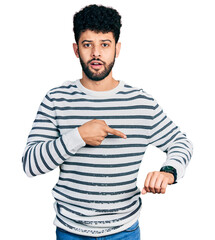 Young arab man with beard wearing casual striped sweater in hurry pointing to watch time, impatience, upset and angry for deadline delay