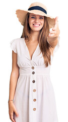 Young beautiful blonde woman wearing summer dress and hat smiling friendly offering handshake as greeting and welcoming. successful business.