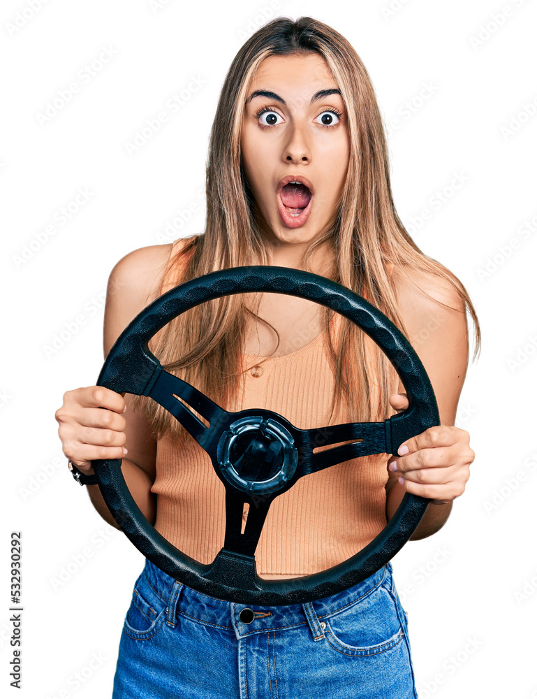 Sticker Hispanic young woman holding steering wheel afraid and shocked with surprise and amazed expression, fear and excited face.