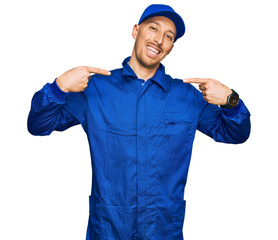 Bald man with beard wearing builder jumpsuit uniform looking confident with smile on face, pointing...