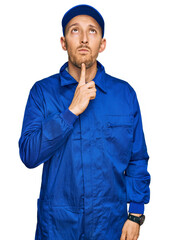Bald man with beard wearing builder jumpsuit uniform thinking concentrated about doubt with finger...