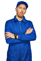 Bald man with beard wearing builder jumpsuit uniform skeptic and nervous, disapproving expression...