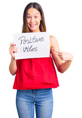 Beautiful brunette young woman holding positive vibes banner smiling happy pointing with hand and finger