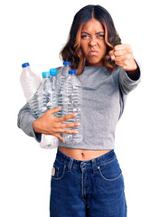 Young beautiful mixed race woman holding recycling plastic bottles annoyed and frustrated shouting with anger, yelling crazy with anger and hand raised