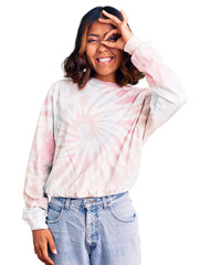 Fototapeta premium Young beautiful mixed race woman wearing casual tie dye sweatshirt doing ok gesture with hand smiling, eye looking through fingers with happy face.