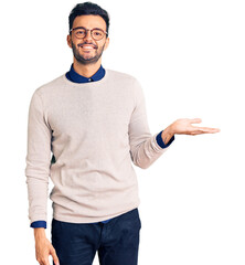 Young handsome hispanic man wearing elegant clothes and glasses smiling cheerful presenting and pointing with palm of hand looking at the camera.