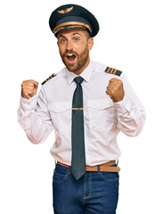 Handsome man with beard wearing airplane pilot uniform celebrating surprised and amazed for success with arms raised and open eyes. winner concept.