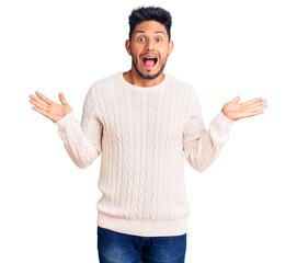 Handsome latin american young man wearing casual winter sweater celebrating victory with happy smile and winner expression with raised hands