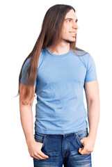 Young adult man with long hair wearing casual clothes looking away to side with smile on face, natural expression. laughing confident.
