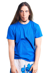 Young adult man with long hair wearing swimwear making fish face with lips, crazy and comical...
