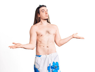 Young adult man with long hair wearing swimwear shirtless clueless and confused expression with...